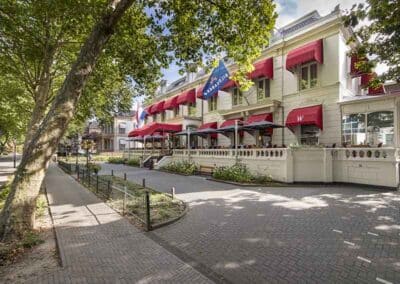 Die Außenansicht des Bilderberg Grand Hotels Wientjes in Zwolle, mit rotem Sonnenschirm und blühenden Bäumen.