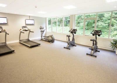 Gut ausgestatteter Fitnessraum im Hotel De Bilderberg in Oosterbeek mit modernen Trainingsgeräten und Blick auf den Wald, für ein aktives und erholsames Aufenthaltserlebnis.
