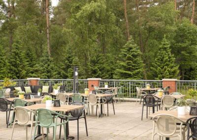 Die einladende Terrasse des Grand Cafés im Bilderberg Residence Groot Heideborgh Hotel, umgeben von der ruhigen Natur der Veluwe, mit modernen Sitzmöglichkeiten und einer idyllischen Aussicht auf den Wald.