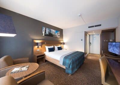 A deluxe room at the Bilderberg Garden Hotel in Amsterdam, featuring a comfortable bed, elegant furniture, and a warm color palette.