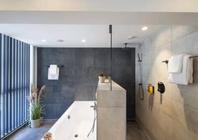 Eine luxuriöse Badezimmer-Suite mit Badewanne und separatem Duschbereich, modernen grauen Fliesen und Meerblick.