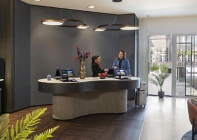 Der Empfangsbereich im Bilderberg Garden Hotel in Amsterdam, mit einem modernen, gebogenen Schreibtisch und Gästen, die einchecken.