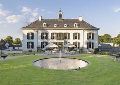 Blick auf die Schlossgarten-Seite des Bilderberg Kasteel Vaalsbroek Hotels, umgeben von üppigem Grün und gepflegten Blumenbeeten.