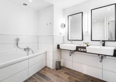 Elegantes Badezimmer im Deluxe-Zimmer des Bilderberg Parkhotel Rotterdam mit modernen Armaturen, großer Dusche, Badewanne und stilvollen Waschbecken.